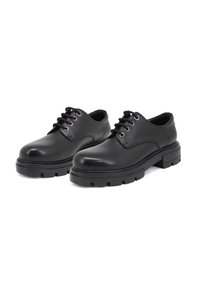 Scarpe in pelle nera con finitura liscia, punta rotonda e sei occhielli per i lacci. Suole in gomma spessa e resistente con un motivo a battistrada.