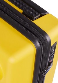 Yellow hard-shell suitcase with black zipper and accents, featuring a textured grip on top and a combination lock on the side.