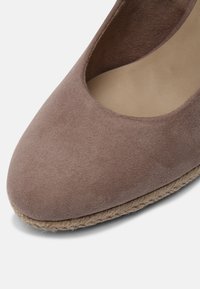 Espadrille en daim avec un bout arrondi, de couleur taupe douce. Présente une semelle en corde naturelle avec un revêtement intérieur lisse.