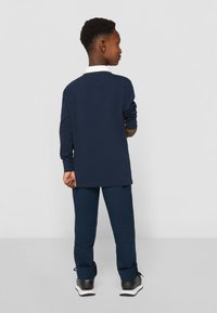 Granatowa koszula z długim rękawem z białym kołnierzykiem, połączona z pasującymi granatowymi spodniami i czarnymi sneakersami. Prosty i casualowy design.