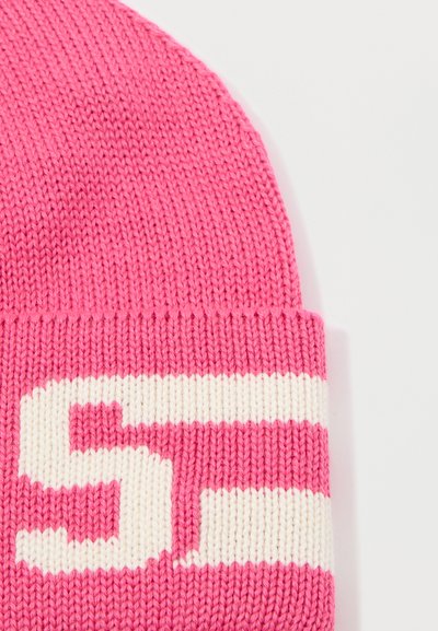 Roze gebreide beanie met een witte gestreepte band en grote witte tekst. De textuur is glad en rekt voor een goede fit.