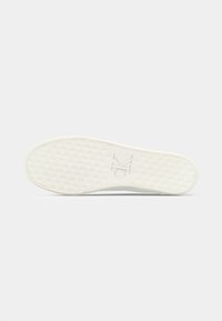 Biała podeszwa sneakersów z teksturowanym wzorem siatki i wytłoczonym logo "CK" na środku, sfotografowana na jasnym białym tle.