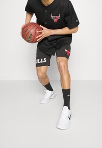 Jersey negro a rayas con el logo de los Bulls, pantalones cortos grises con el texto "BULLS", zapatillas blancas y calcetines negros, sosteniendo un balón de baloncesto.
