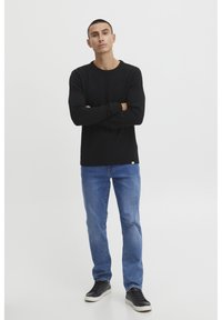 Black long-sleeve knit sweater paired with light blue straight-leg jeans and black sneakers. Simple design with ribbed cuffs and hem.