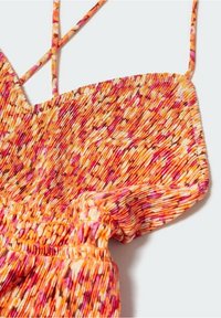 Gros plan d’une robe en tissu coloré et texturé avec de fines bretelles et une taille élastique dans des tons orange, rose et blanc.