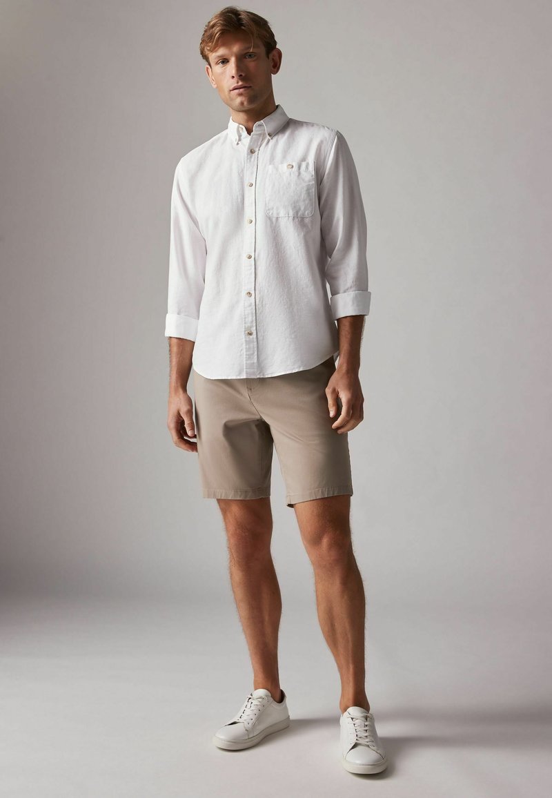 Chemise blanche à manches longues, shorts beige et baskets blanches. Complète un design simple et décontracté avec une texture de tissu léger.