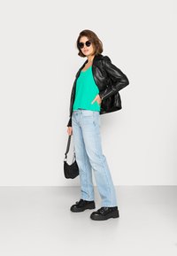 Jaqueta de couro preta, blusa verde sem mangas, jeans azul claro de perna reta, sapatos plataforma pretos, pequena bolsa preta, óculos de sol redondos.