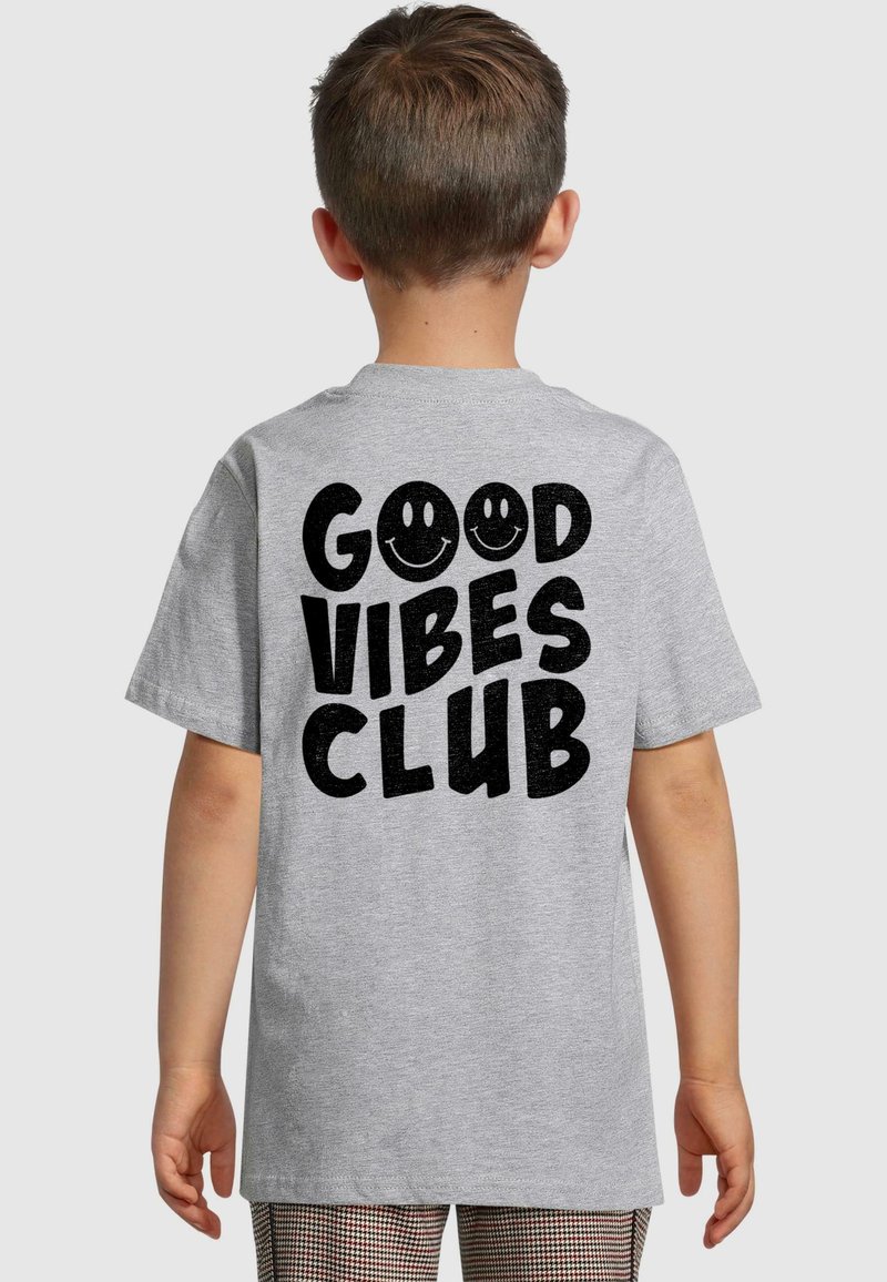 Šedé tričko s krátkým rukávem s výrazným černým textem "GOOD VIBES CLUB" a dvěma usmívajícími se tvářemi na zadní straně. Měkký bavlněný materiál.