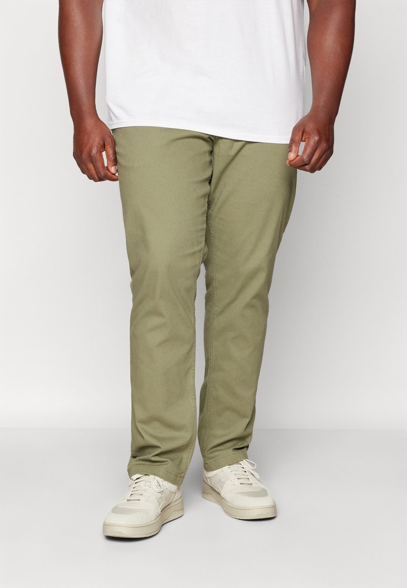Pantalones de algodón de color verde oliva con un diseño de pierna recta, que cuentan con bolsillos frontales y una textura suave, usados con zapatillas de color claro.
