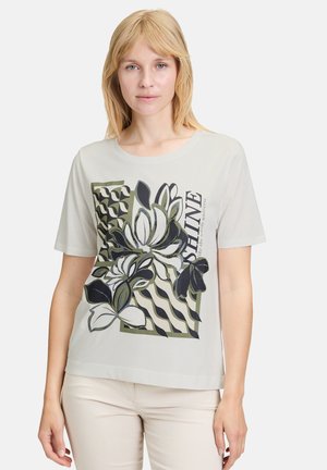 T-shirt gris clair avec un graphique floral en noir et vert, accompagné de motifs géométriques et du mot "SHINE" dans une police moderne.