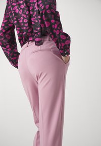 Pink tailored pants with a smooth texture and pockets, paired with a black blouse featuring a vibrant pink lip pattern.