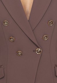 Blazer marrone doppiopetto con bottoni in tonalità oro, caratterizzato da un profondo scollo a V e un tessuto testurizzato. Include tasche laterali.