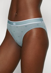 Gaiši zila sieviešu apakšbikses ar mīkstu tekstūru, ar baltu jostu un diskretu atkārtotu logo rakstu. Klasiska liela griezuma dizains.