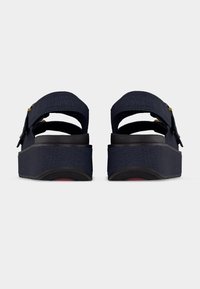 Πλατφόρμες σε ναυτικό μπλε με ρυθμιζόμενα λουράκια αστραγάλου και χοντρές μαύρες σόλες, εμφανιζόμενες από πίσω σε απλό λευκό φόντο.