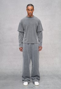 Grijs oversized lang overhemd met gelaagde korte mouwen, gecombineerd met een bijpassende losse broek, beiden in zachte fluwelen stof. Witte sneakers.