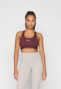 Bordeaux sportbeha met brede banden en een wit logo aan de voorkant, gecombineerd met lichtbeige high-waisted leggings. Gladde textuur, aansluitend ontwerp.
