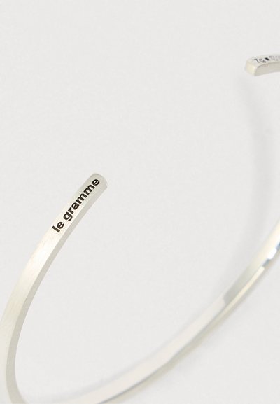 Plāns sudraba rokassprādze ar iegravētu tekstu "le gramme" uz gala, novietota uz vienkārša gaiša fona.