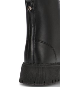 Botín negro de cuero con suela de goma texturizada, que presenta un acento metálico y costuras en el lateral.