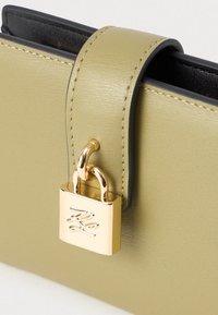 Κοντινό πλάνο από ανοιχτό πράσινο δερμάτινο πορτοφόλι με ραμμένες άκρες και μια μικρή χρυσή λουκέτα προσαρτημένη σε μια θήκη.