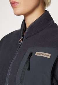 Tume navy fleece-jakk, millel on lukuga rinna tasku, logopatch ja kõrge kaelus; pehme tekstuur ja keha järgi disain.