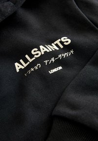 Sort sweatshirt med hvid tekst: "ALLSAINTS," japanske tegn og "LONDON." Glat stof med ribbede manchetter.