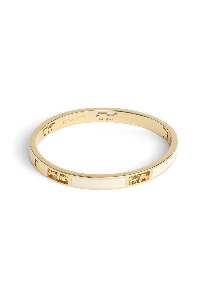 Guldtonad bangle-armband med växlande vita emaljrandar och utskurna mönster, som har en slät, jämn textur och en minimalistisk form.