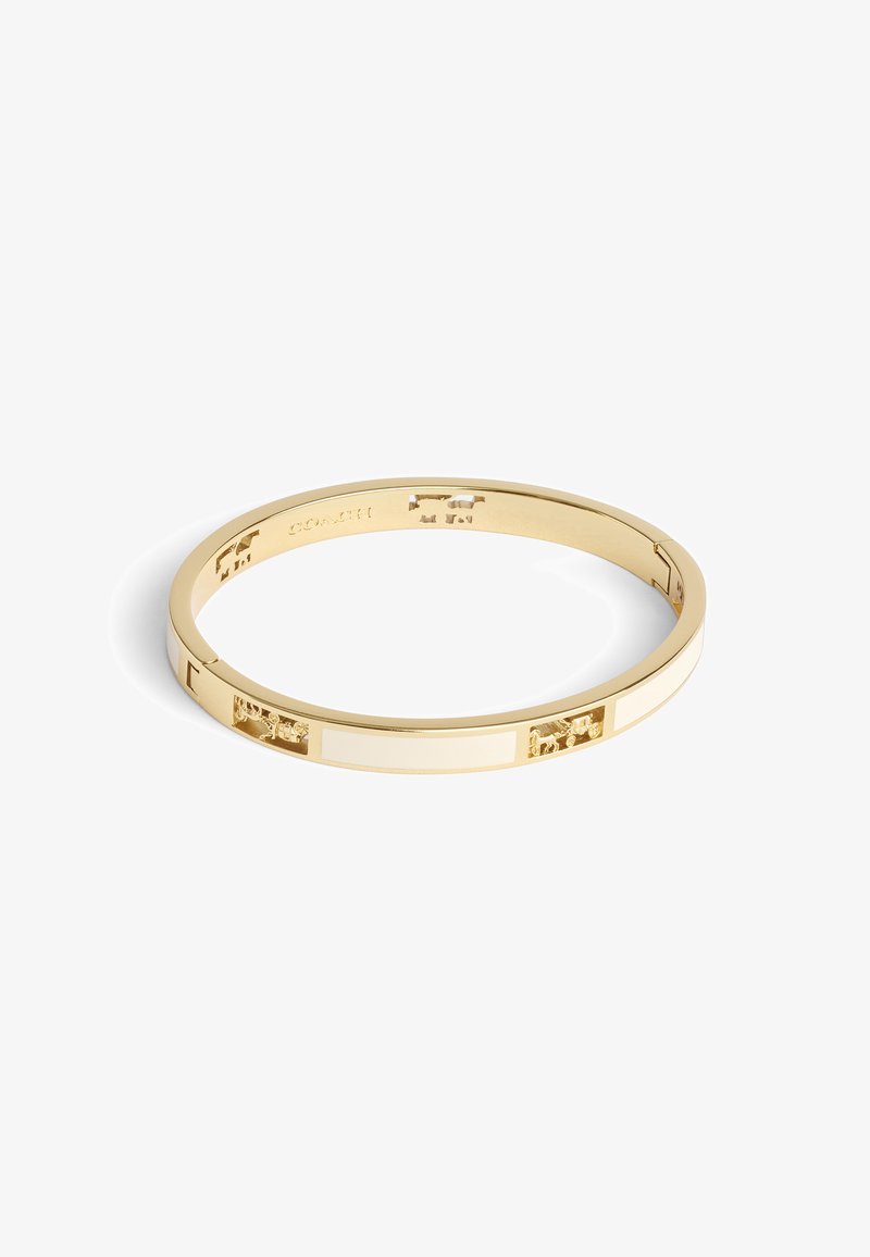 Guldtonad bangle-armband med växlande vita emaljrandar och utskurna mönster, som har en slät, jämn textur och en minimalistisk form.