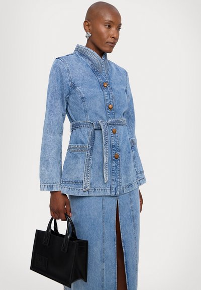 Denimjakke med belte i midjen, lyseblå farge, knappert front, lommer, paret med et matchende skjørt og en svart håndveske.