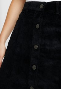 Zwarte corduroy rok met een a-lijn ontwerp, gestructureerde stof, sluiting met knopen aan de voorkant met metallic accenten, en zijzakken.