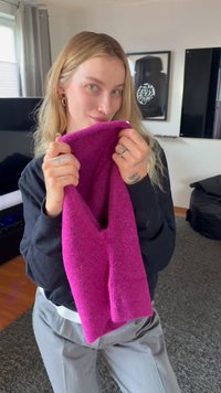 Νεαρή γυναίκα με ξανθά μαλλιά που κρατά ένα απαλό, φωτεινό ροζ ύφασμα κοντά στο πρόσωπό της σε ένα καθιστικό.