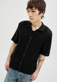 Black short-sleeve polo shirt in textured knit with a collar and buttoned front, paired with light blue denim shorts. Minimalist design.