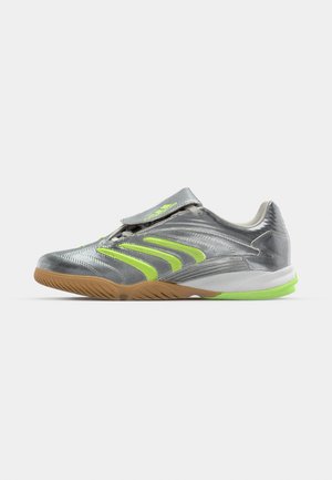 Zapatilla atlética gris con detalles en verde neón, con una textura superior suave, correa ajustable y suela de goma.