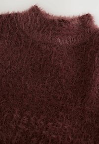 Burgunderröd tröja med en fluffig textur och en hög krage, med ett subtilt mönster över hela tyget. Lätt och mjuk känsla.