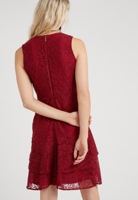Robe en dentelle rouge avec un design à volants et des motifs floraux, sans manches, et une fermeture éclair au dos. Tissu texturé.