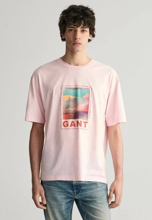 Camiseta de algodón rosa, de corte relajado, con un estampado gráfico colorido que incluye el texto "GANT". Diseño de mangas cortas y cuello redondo.