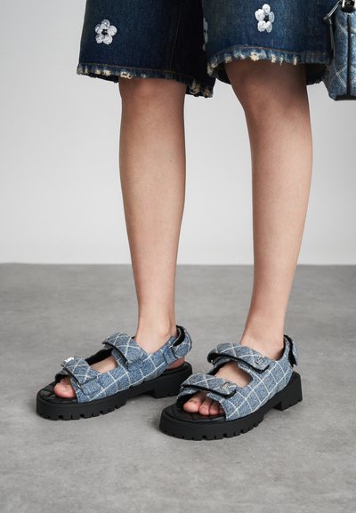 Farmertapós szandál, kockás mintával, két állítható pánttal és vastag fekete gumitalppal. Nyitott orrész, texturált kiegészítőkkel.