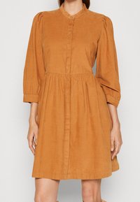Vestito a maniche corte, senza colletto, in velluto a coste color arancione sabbia, con chiusura a bottoni sul davanti e vita arricciata, dalla vestibilità rilassata.