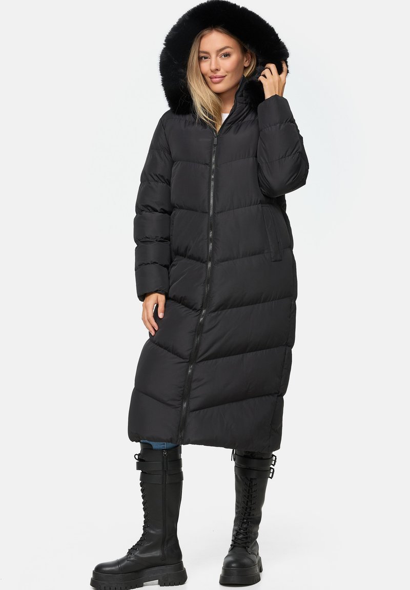 Cappotto puffer nero con cappuccio foderato in pelliccia, design lungo, chiusura con zip e texture trapuntata. Abbinato a stivali combat neri.