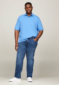 Polo azzurro chiaro in cotone, con colletto e maniche corte, abbinato a jeans blu scuro e sneakers bianche.