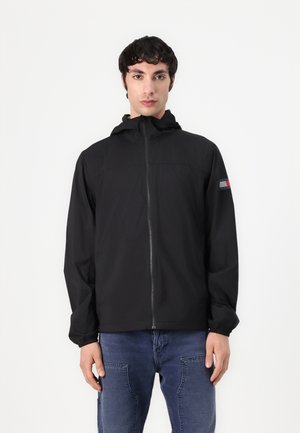 Zwarte lichtgewicht jas met capuchon, volledige ritssluiting aan de voorkant, elastische manchetten en een merkaccent in rood en blauw op de linker mouw.