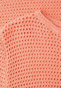 Tissu tricoté rose corail avec une texture gaufrée et un gros plan sur le bord arrondi de l'encolure.