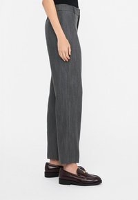 Pantaloni larghi grigi con una texture liscia e sottili righe verticali; abbinati a mocassini bordeaux scuri con dettagli in oro.