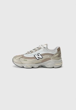 Beige og hvide New Balance 1100 sneakers med mesh og læderdetaljer, snørebånd og tyk gummisål set fra siden.