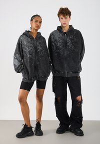 Hanorace negre supradimensionate cu fermoar au modele cu puncte metalice pe față. Asortate cu blugi negri rupți și adidași sport.