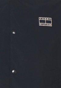 Camicia blu navy con bottoni realizzata in tessuto con finitura testurizzata, con una toppa del logo Tommy Hilfiger ricamata in bianco e nero sul petto.
