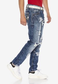 Denim-Jeans in einem ausgewaschenen, verwaschenen Blauton. Mit Rissen und Kontrastnähten. Kombiniert mit weißen Sneakers.