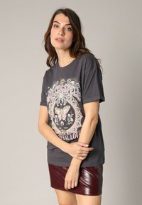 Camiseta gráfica gris con un diseño de mariposa y acentos florales en rosa y crema. Combinada con una falda de cuero brillante burdeos.