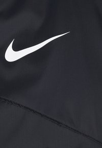 Svart Nike-tyg med en framträdande vit swoosh-logotyp. Materialet verkar vara slätt med en subtil glans och sömnadsdetaljer.