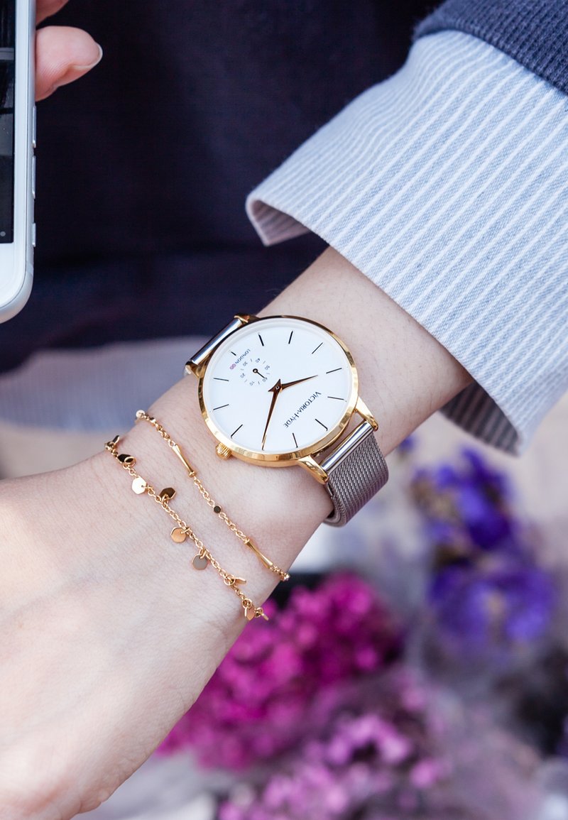 Kultakäyttöinen kello valkoisella kellotaululla, verkkohihnalla ja mustilla tunnusmerkeillä. Mukana on herkkä kultaketju sydänkoristeluilla.