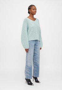 Ljusblå stickad tröja med vida ärmar, kombinerad med högmidjade urtvättade jeans. Modellen bär spetsiga svarta ankelstövlar med silverfärgade tådetaljer.
